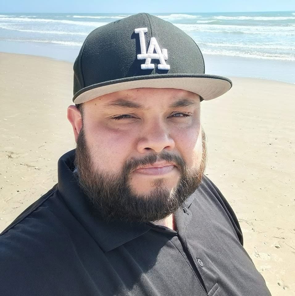 Michael at the beach, in a black LA cap, the surf behind Him.