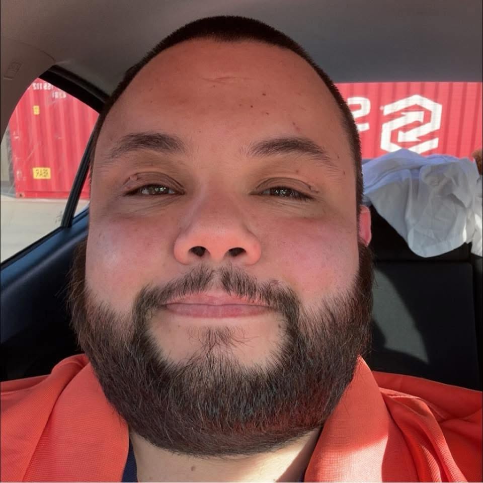 Close-up portrait of Michael in a vehicle, an industrial yard behind him.